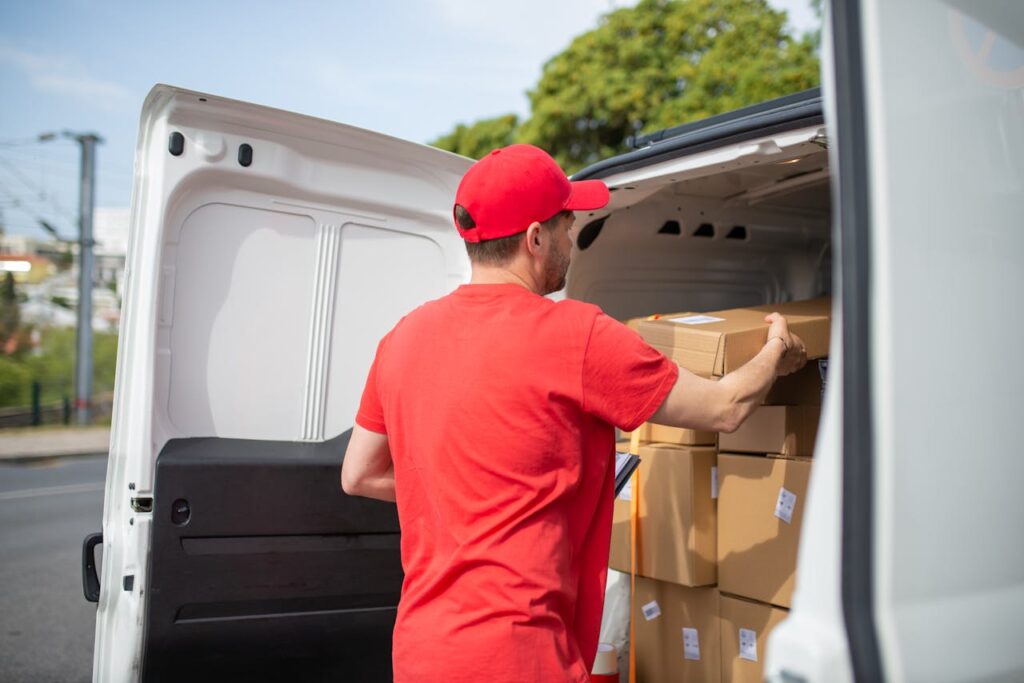 Courier carrying packages into a van for delivery, wearing a red uniform.